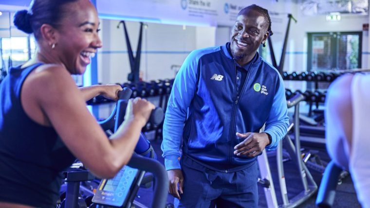 Man in The Gym Group uniform smiling at a woman on an exercise bike.