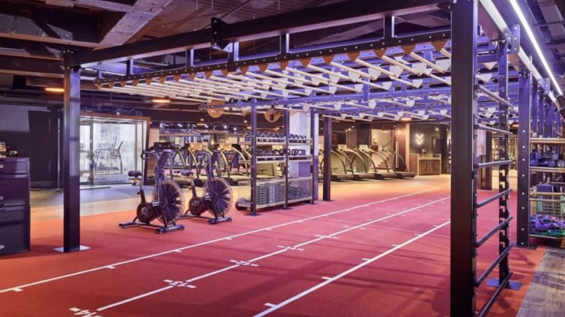Modern gym interior with red track, workout equipment, treadmills, and monkey bars, representing a Third Space fitness fac...