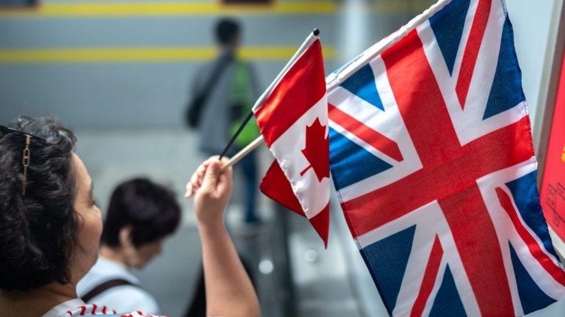 A person holds small UK and Canadian flags, symbolizing international relations.