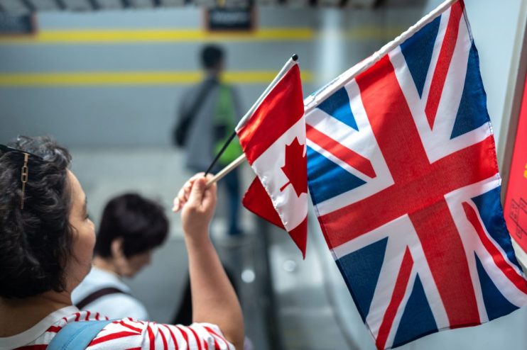 A person holds small UK and Canadian flags, symbolizing international relations.