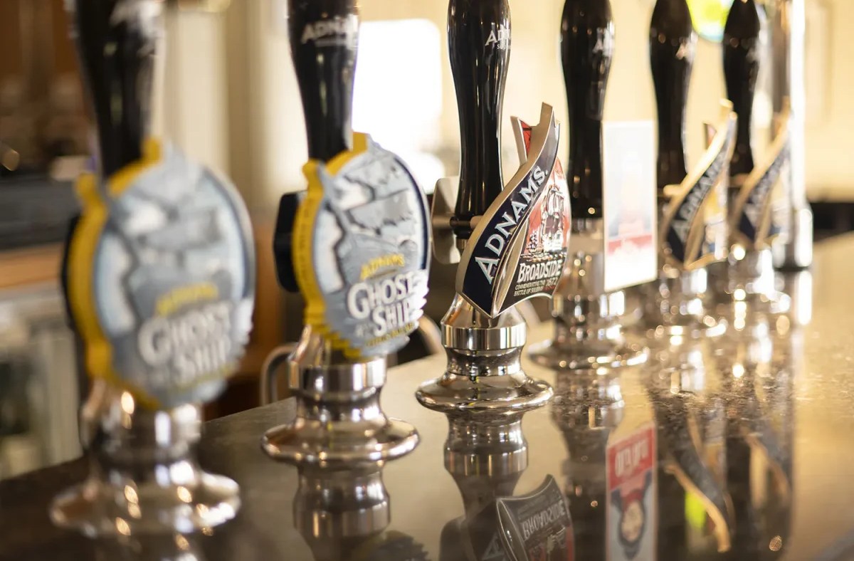 Adnams beer pumps lined up on a bar, with Broadside and Ghost Ship visible on the handles.