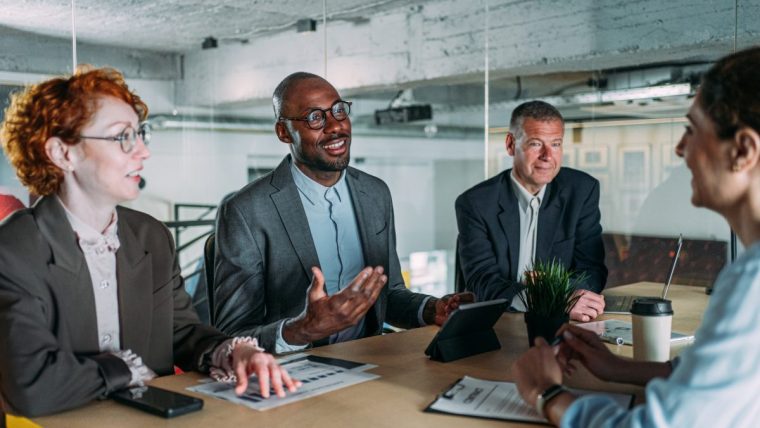 Diverse business professionals in a modern office meeting, discussing strategies with a tablet and documents.