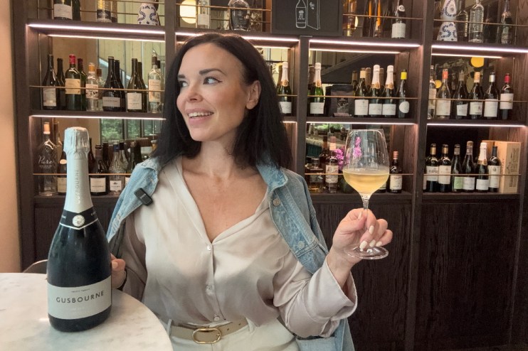 Woman smiling, holding a wine glass and standing next to a Gusbourne sparkling wine bottle at Daves Wine Bar.