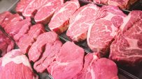 Assortment of fresh red meat cuts, including steaks and roasts, displayed in a butcher shop or supermarket cooler.