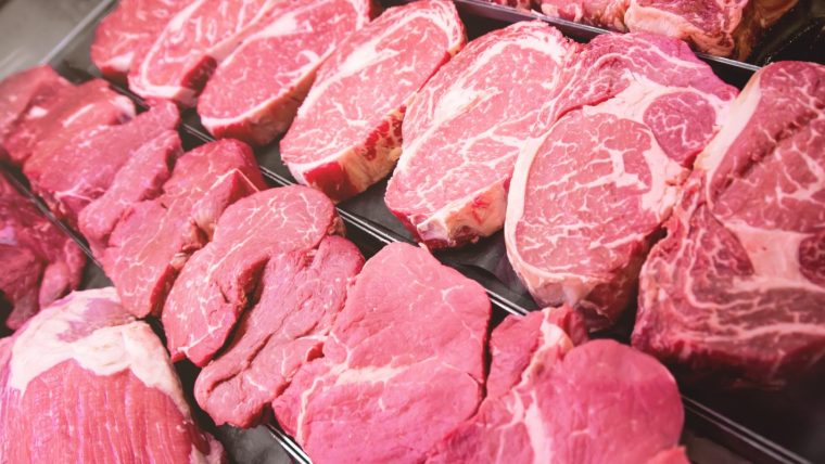 Assortment of fresh red meat cuts, including steaks and roasts, displayed in a butcher shop or supermarket cooler.