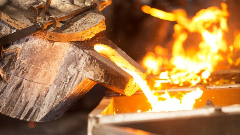 Molten metal pouring from a crucible into a mold, glowing orange in a metallurgy foundry.
