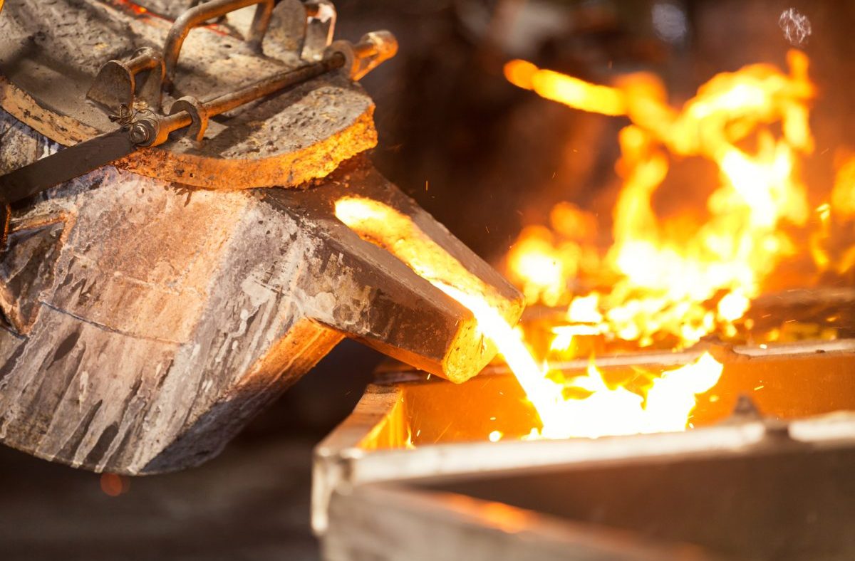 Molten metal pouring from a crucible into a mold, glowing orange in a metallurgy foundry.
