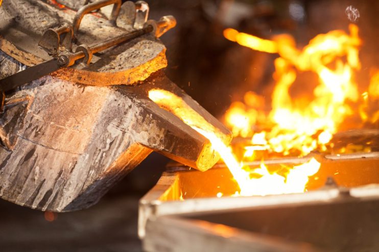 Molten metal pouring from a crucible into a mold, glowing orange in a metallurgy foundry.
