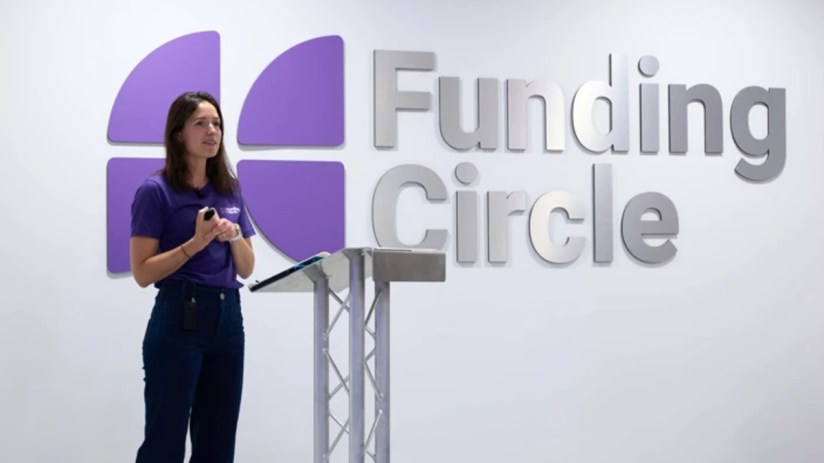 Woman in purple shirt speaking at a podium with Funding Circle logo on the wall