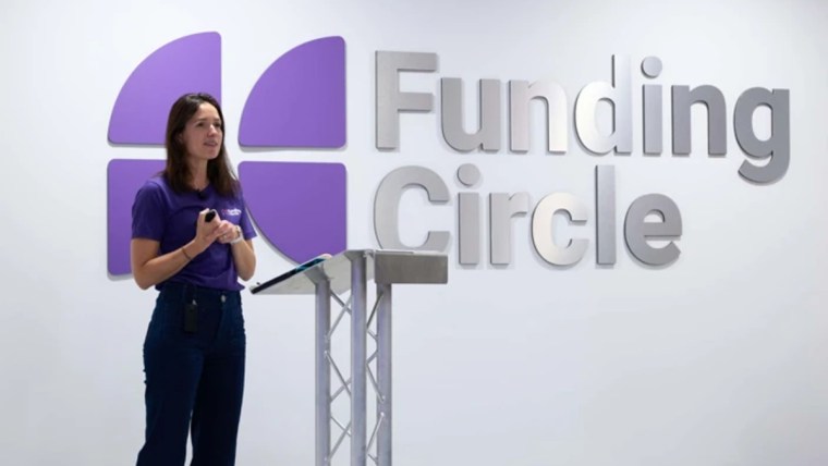 Woman in purple shirt speaking at a podium with Funding Circle logo on the wall