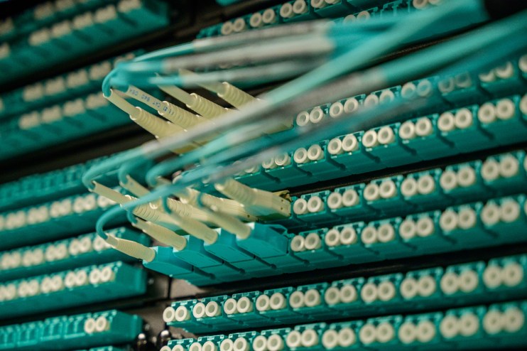 Close-up of fiber optic cables and connectors in a server rack, illustrating data center technology and connectivity.
