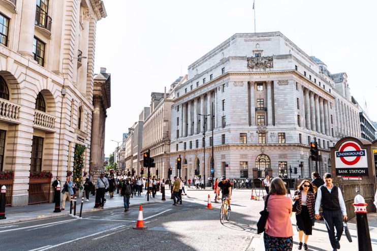 Busy street scene in London with historic buildings, pedestrians, traffic, and a Bank Underground station sign.