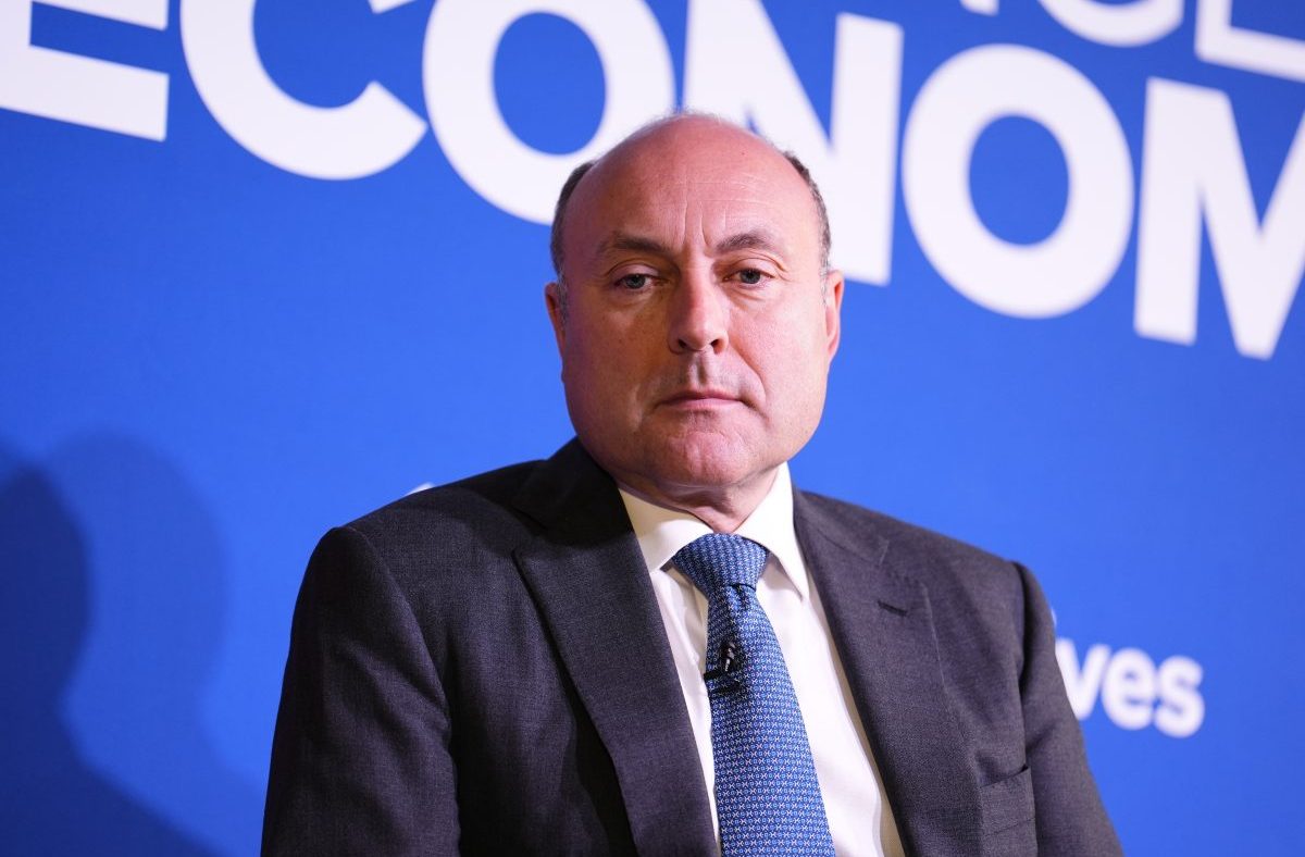 Shadow Chancellor Andrew Griffith in a suit and patterned blue tie, against a blue background with white text.