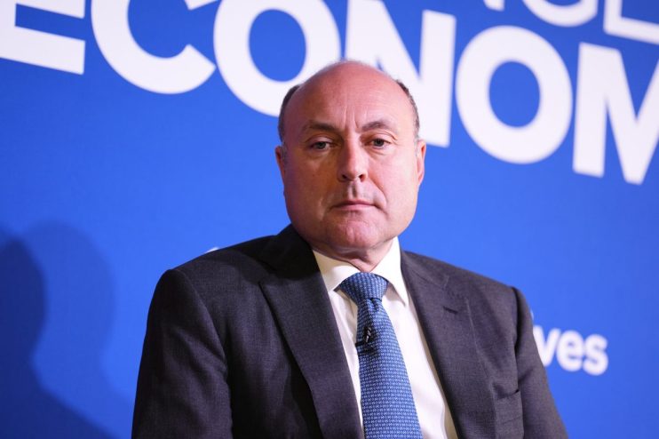 Shadow Chancellor Andrew Griffith in a suit and patterned blue tie, against a blue background with white text.