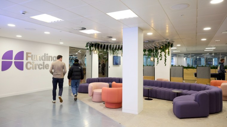 Two men walk past the Funding Circle logo in a modern office lounge area with purple and pink seating.