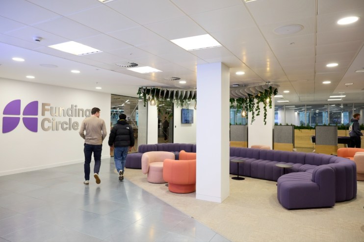 Two men walk past the Funding Circle logo in a modern office lounge area with purple and pink seating.